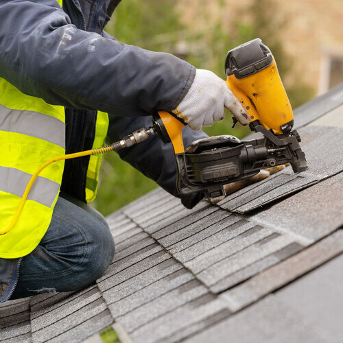 worker nailing down shingles